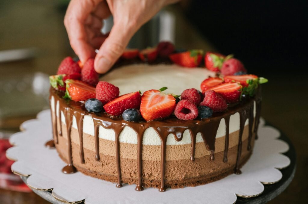Hand decorating a chocolate layer cake with fresh berries and cream frosting.